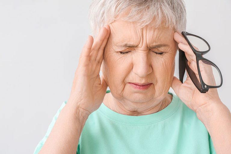 stressed senior woman suffering headache light background