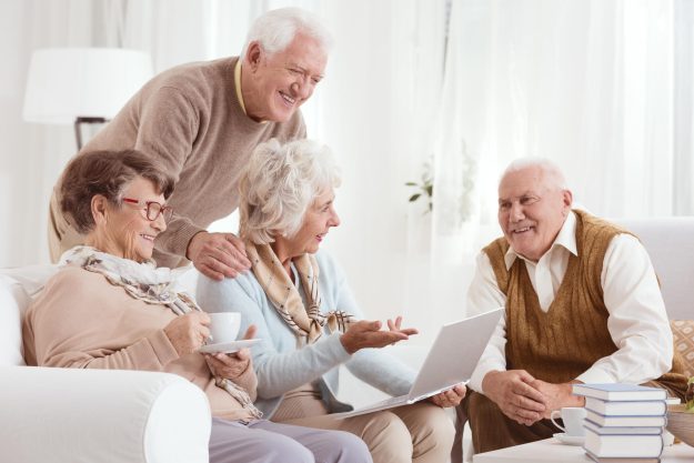 Group,Of,Senior,Friends,Converses,While,Using,Laptop,In,Living Group,Of,Senior,Friends,Converses,While,Using,Laptop,In,Living