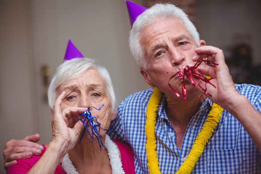 Close up portrait of senior couple blowing party horn at home
