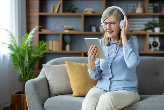 Elderly woman enjoying technology, listening to music or a podcast with headphones and using a tablet.— Photo Elderly woman enjoying technology, listening to music or a podcast with headphones and using a tablet.— Photo
