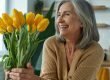 Elegant senior woman holding a bunch of yellow tulips and smiling while relaxing at home