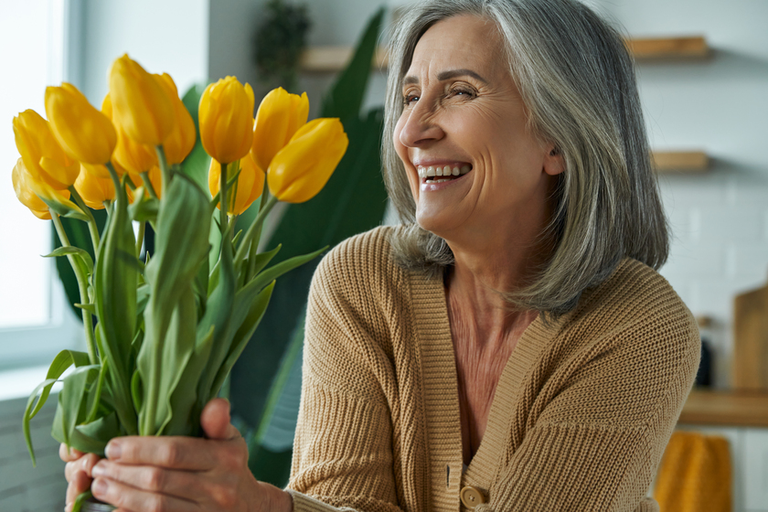 Elegant senior woman holding a bunch of yellow tulips and smiling while relaxing at home Elegant senior woman holding a bunch of yellow tulips and smiling while relaxing at home