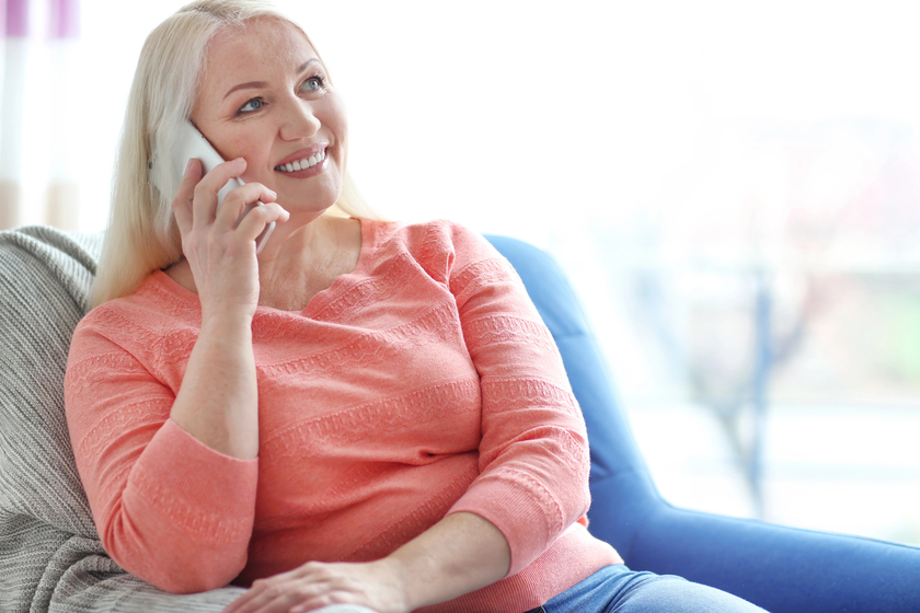 Happy mature woman talking on phone while sitting in armchair at home Happy mature woman talking on phone while sitting in armchair at home