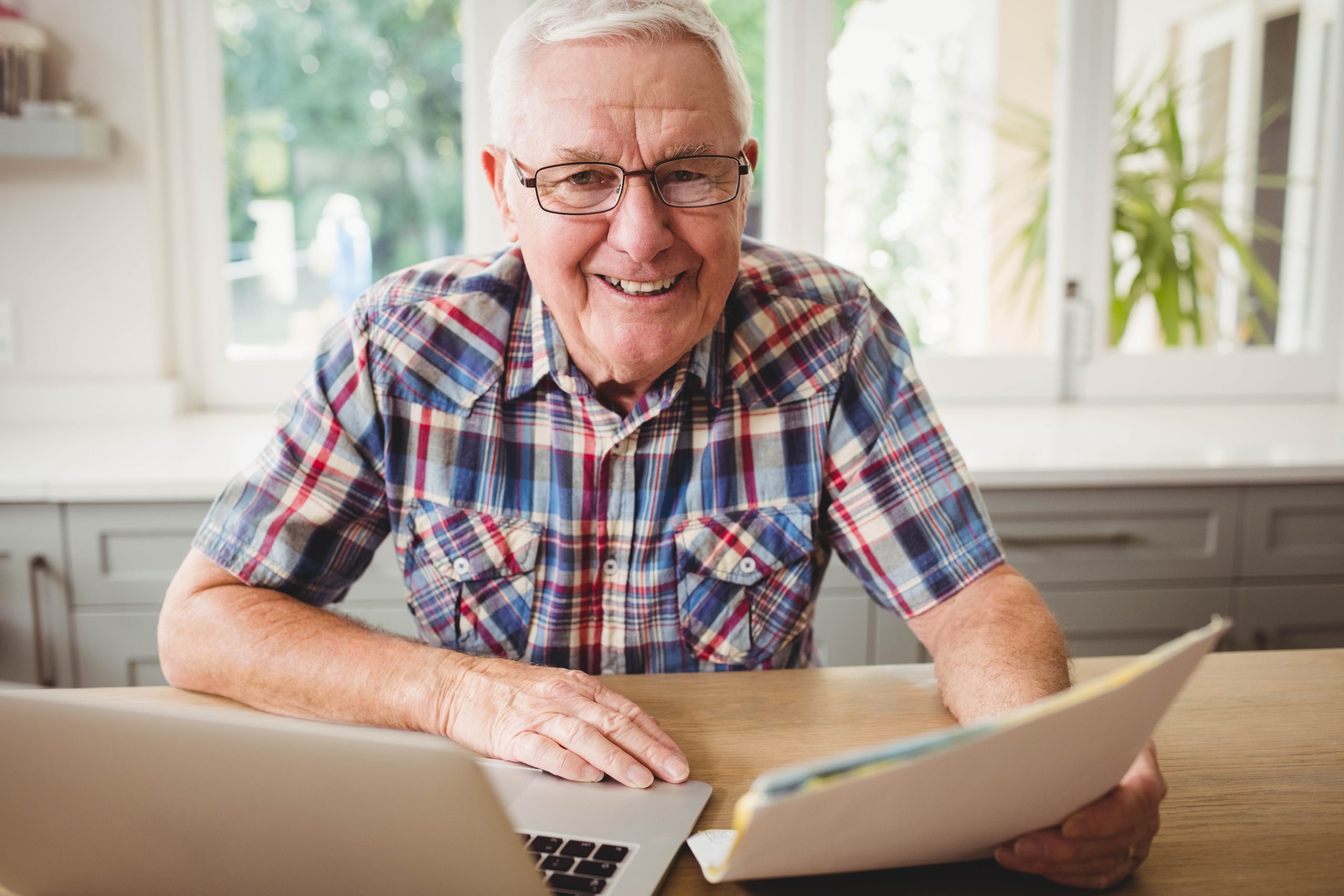 Happy senior man holding a document while using laptop at home Happy senior man holding a document while using laptop at home