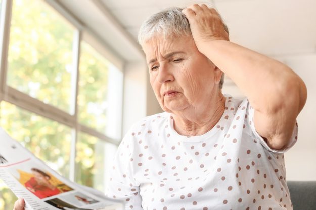 Stressed senior woman reading newspaper at home