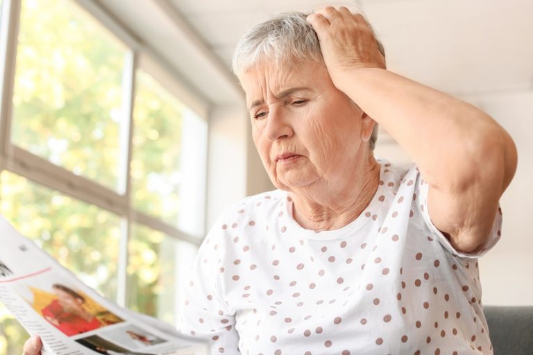 Stressed senior woman reading newspaper at home