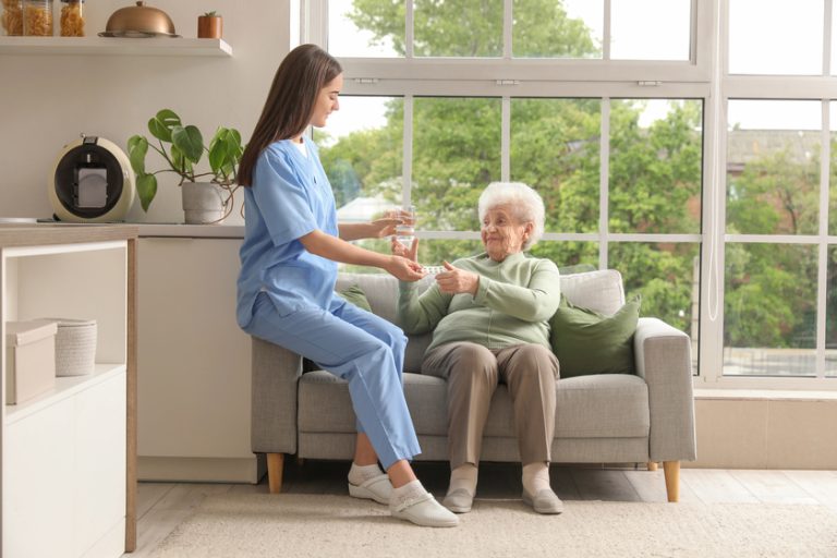 Young nurse giving pills and glass of water to senior woman in kitchen — Photo