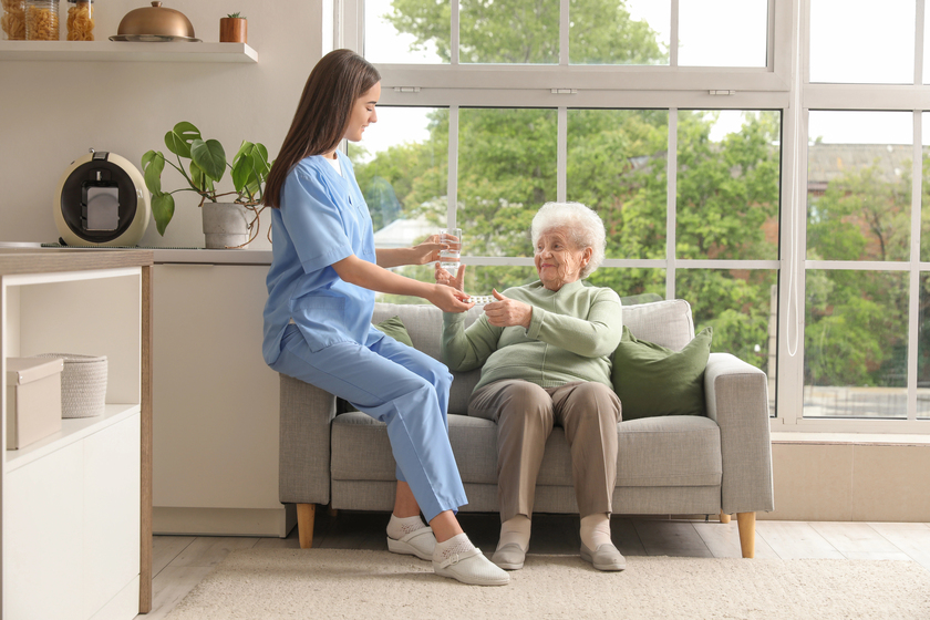 Young nurse giving pills and glass of water to senior woman in kitchen — Photo