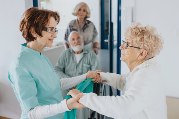 Smiling,Nurse,Holds,An,Elderly,Lady’s,Hands,,Helping,Her Smiling,Nurse,Holds,An,Elderly,Lady's,Hands,,Helping,Her