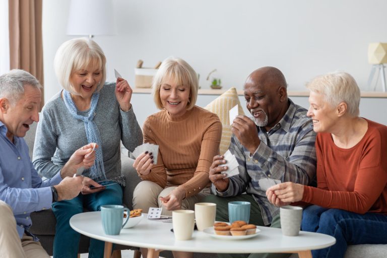 Happy senior friends playing cards while chilling together at home