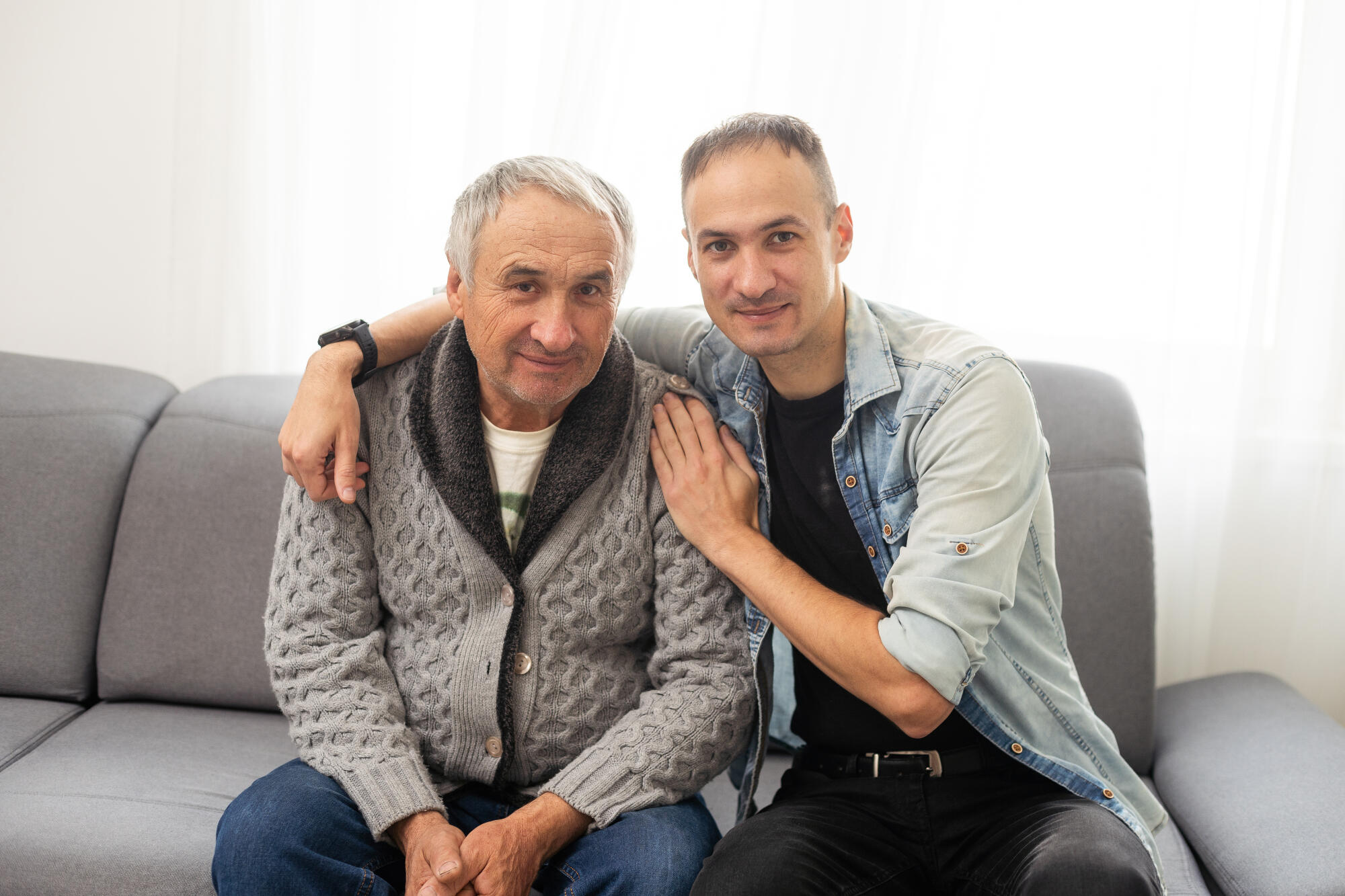 Grown up son asking for apologizes to offended stressed elderly senior daddy, sitting together on couch. Compassionate young man supporting, giving psychological help to frustrated middle aged father.