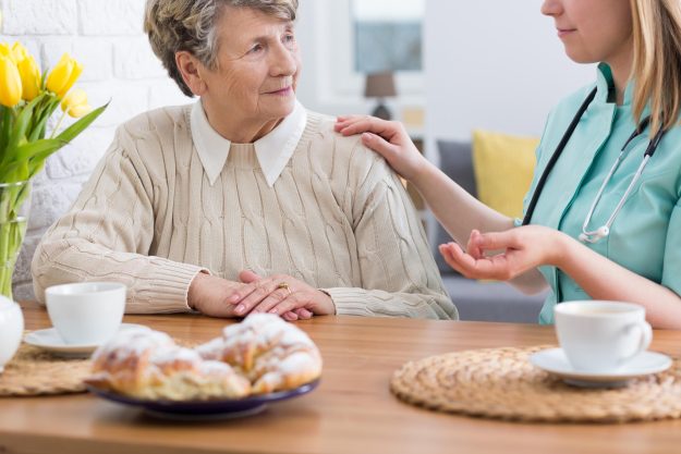 Senior,Lady,Sitting,At,A,Table,With,Her,Home,Nurse,