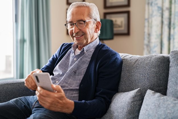 Smiling,Old,Man,Using,Smartphone,While,Sitting,On,Couch.,Happy Smiling,Old,Man,Using,Smartphone,While,Sitting,On,Couch.,Happy