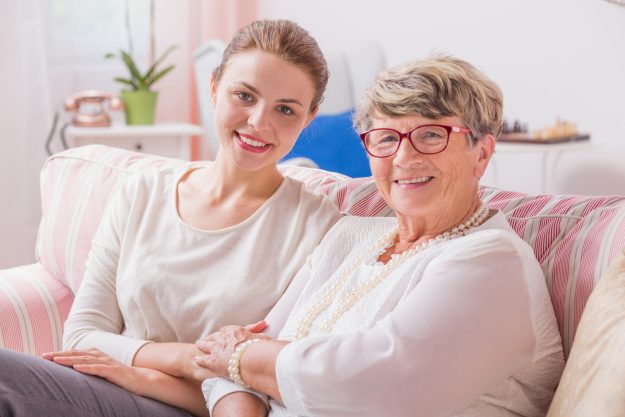 Elder,Woman,Sitting,On,A,Couch,With,Her,Young,Granddaughter