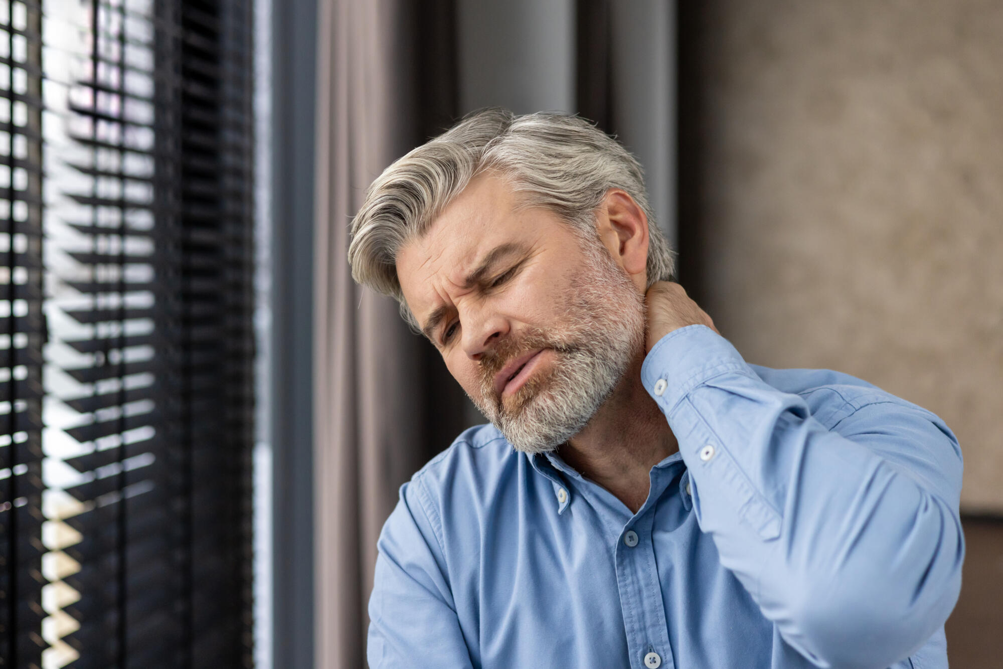 Middle aged businessman experiencing neck pain in office setting Middle aged businessman experiencing neck pain in office setting