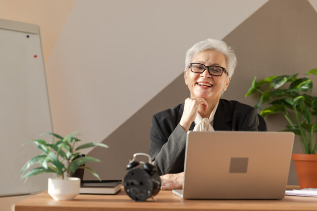 Portrait of confident stylish european middle aged senior woman at workplace. Stylish older mature 60s gray haired lady businesswoman sitting in modern office. Boss leader teacher professional worker.