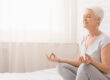 Senior woman doing yoga on bed at home