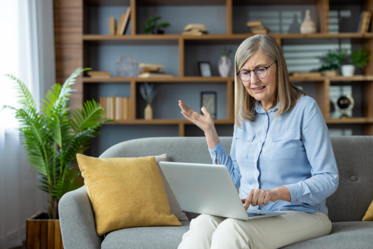 Frustrated senior woman experiencing computer issues while working from home on a laptop