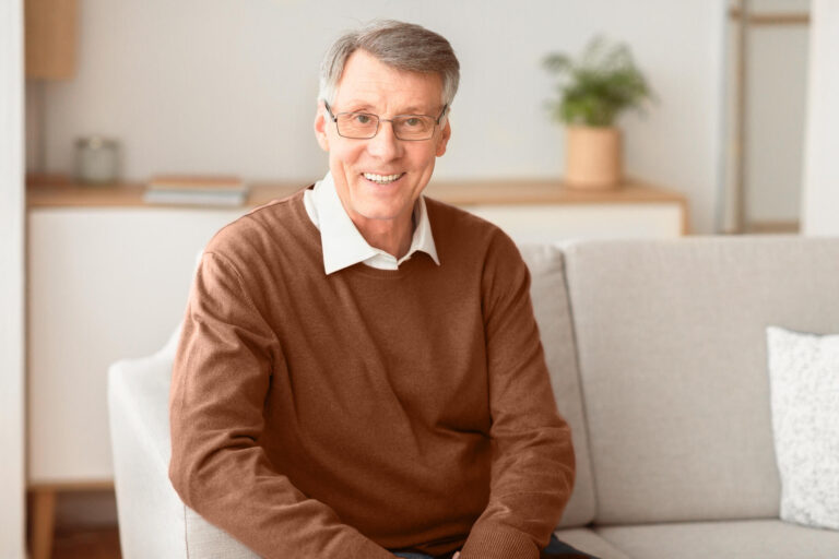 Smiling Senior Gentleman Sitting On Couch At Home
