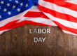 words labor day laid with silver metal letters on wooden surface with crumpled USA flag on upper side