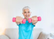 Senior woman exercising with dumbbells at home. Sporty beautiful woman exercising at home to stay fit. Elderly woman exercising at home in a living room. Fitness, workout, healthy living and diet concept.