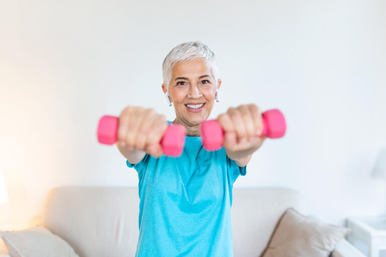 Senior woman exercising with dumbbells at home. Sporty beautiful woman exercising at home to stay fit. Elderly woman exercising at home in a living room. Fitness, workout, healthy living and diet concept.
